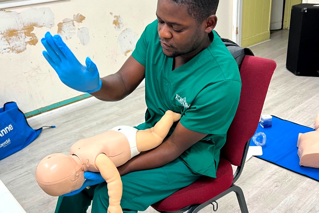 Instructor demonstrating infant back blows while seated with a training manikin