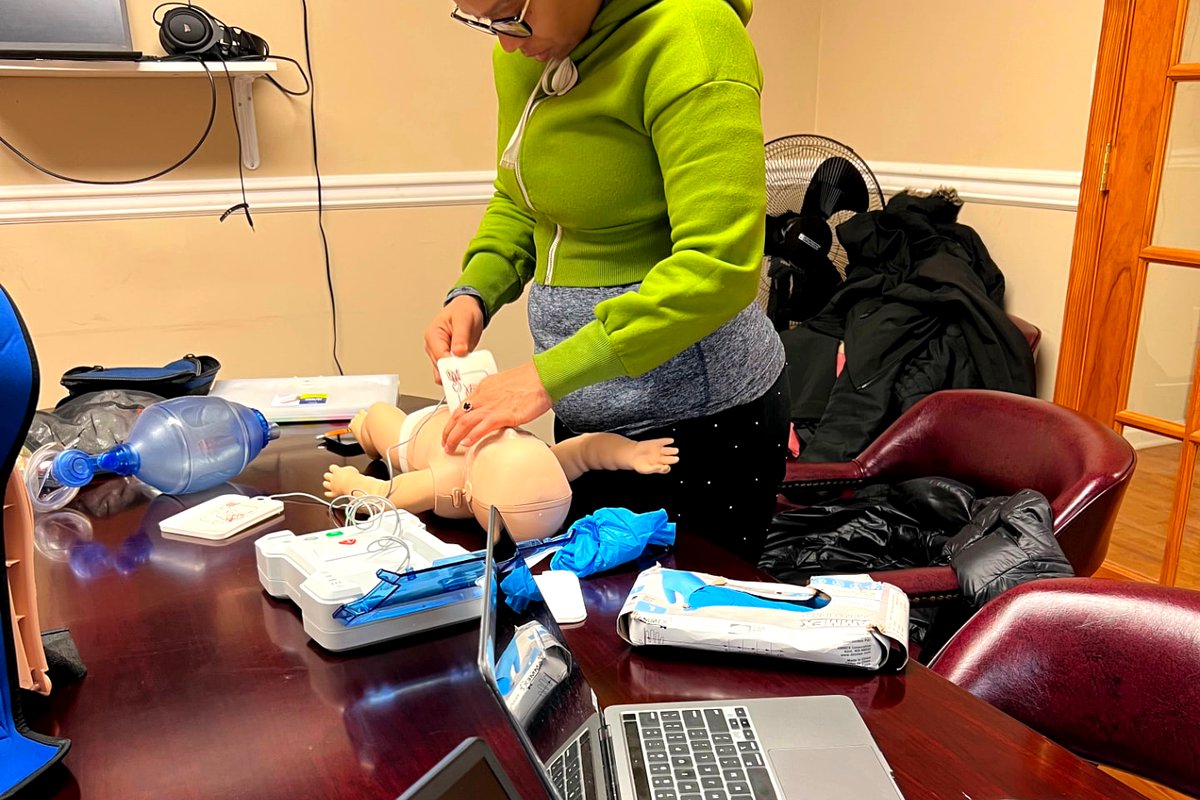 Learner applying AED pads to an infant manikin with a bag valve mask on the table