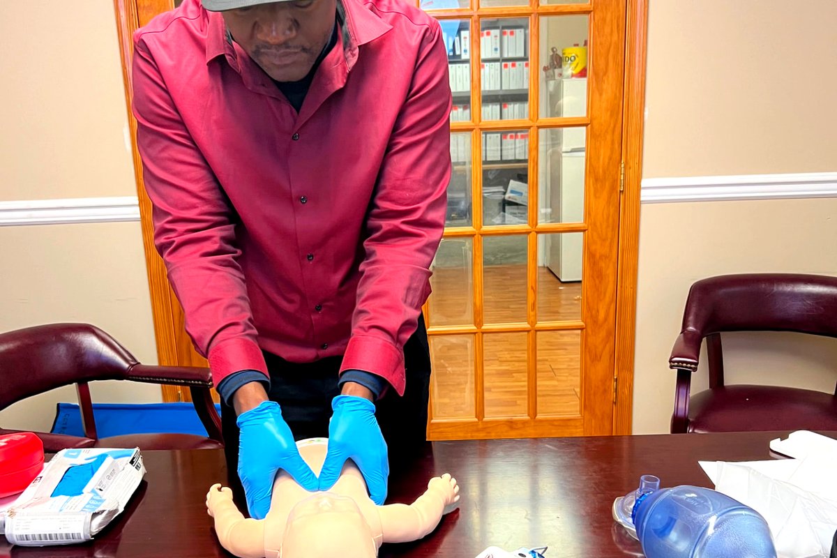 Learner performing two thumb infant CPR on a manikin with AED and bag valve mask equipment nearby